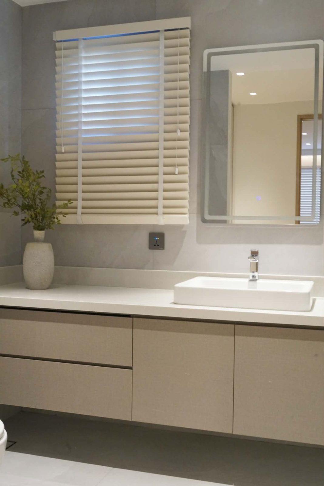 Bathroom vanity with greige drawers, a white basin and a backlit mirror